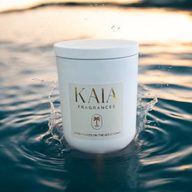A white candle called 'coastal rain' sitting in water that has slashed up on the candle with a sunset in the background