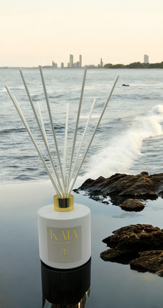 A white reed diffuser sitting on water with the ocean and buildings in the background