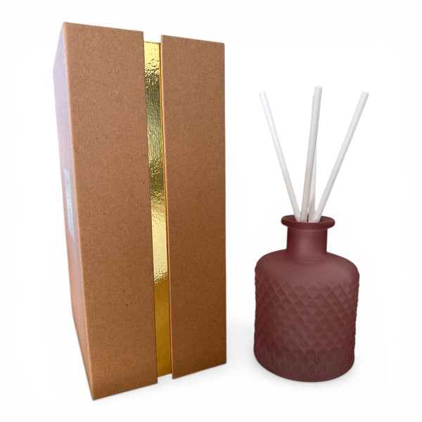Brown textured diffuser box with pink diffuser bottle and white sticks and gold accent on a white background