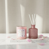 Pink candle with KAIA label and diffuser with floral design on a marble surface with pink petals.