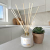 Reed diffuser with 'KAIA' branding on a kitchen counter with a plant in the background