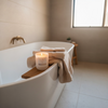 KAIA Unwind coco soy candle Bathroom scene with a bathtub, candle, and towels.