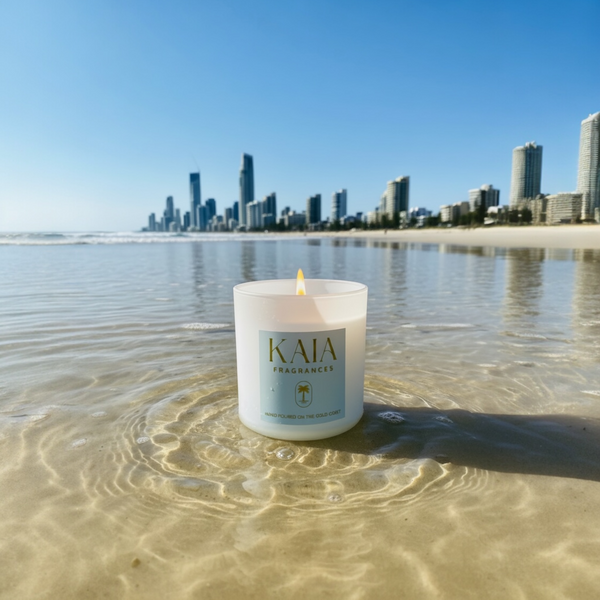 Candle labeled 'KAIA' on a beach with a city skyline in the background