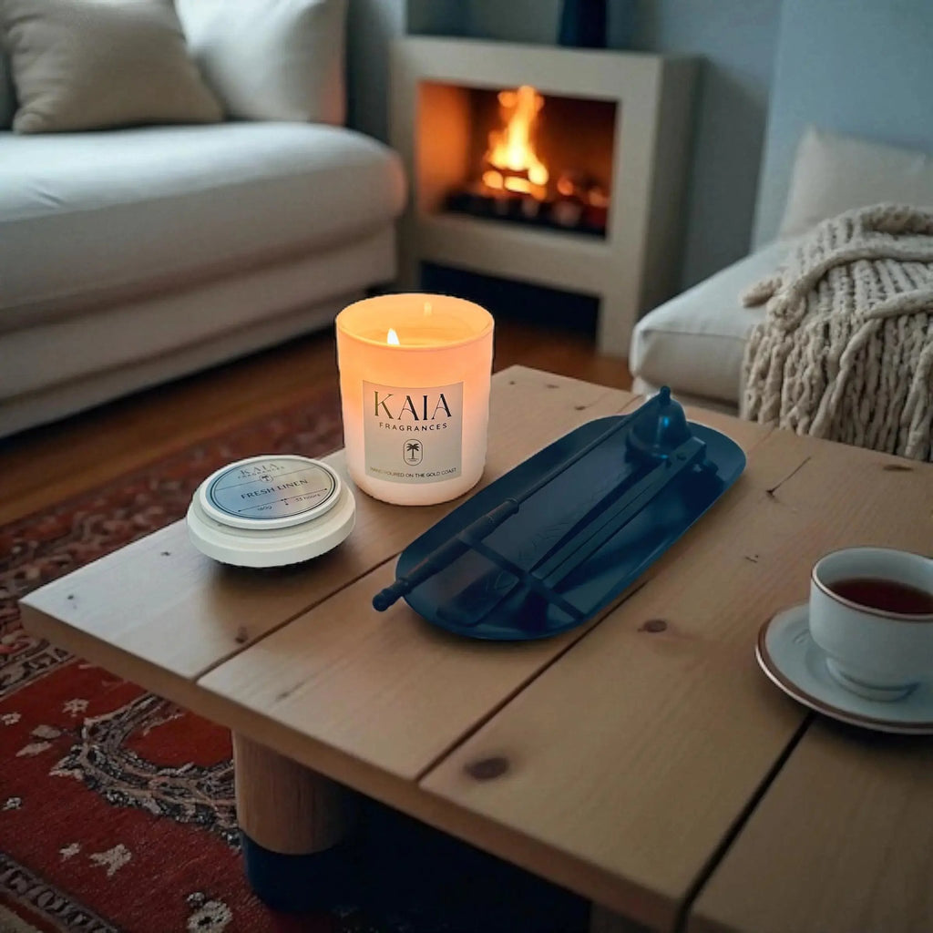 Candle labeled 'KAIA' with candle care kit on a wooden table with a cozy living room background